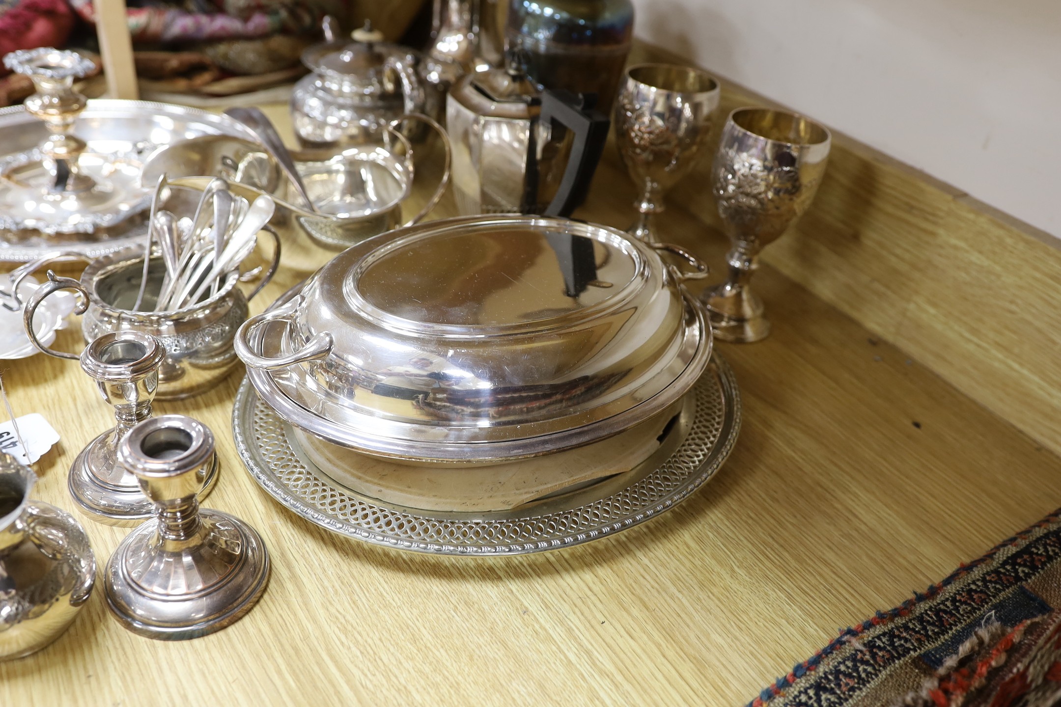 A quantity of assorted plated wares including a chamberstick, a tea set, flatware, a cocktail shaker, a sauceboat, goblets, etc.